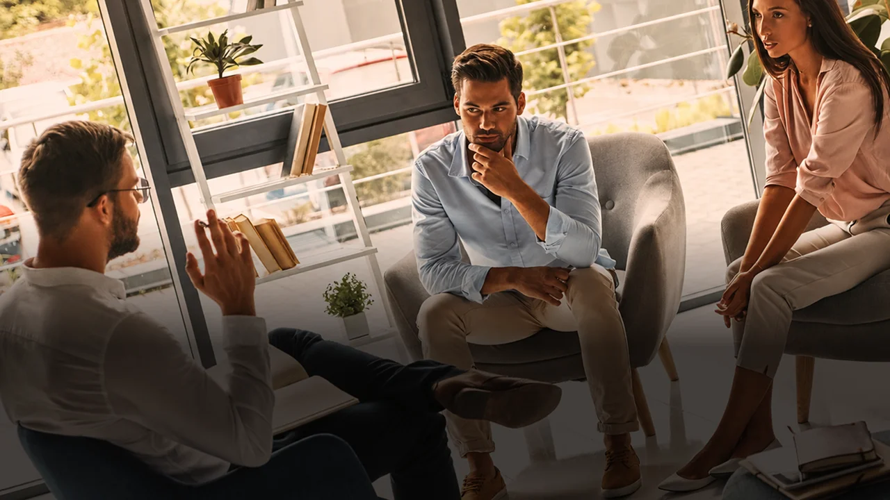 A professional speaking with a couple sitting in armchairs during a consultation session in a bright office.